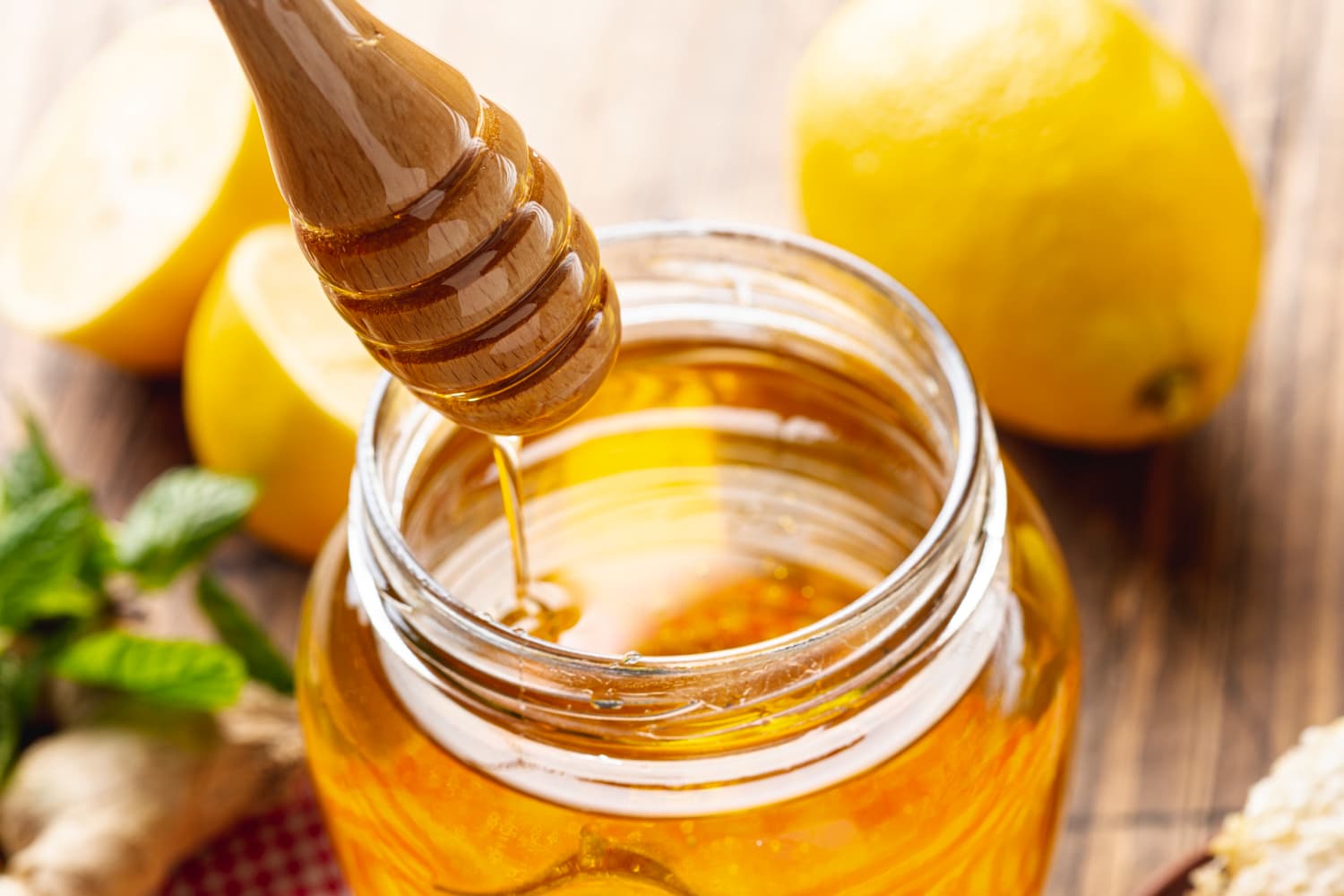 Honey dipper dripping into an open jar of honey